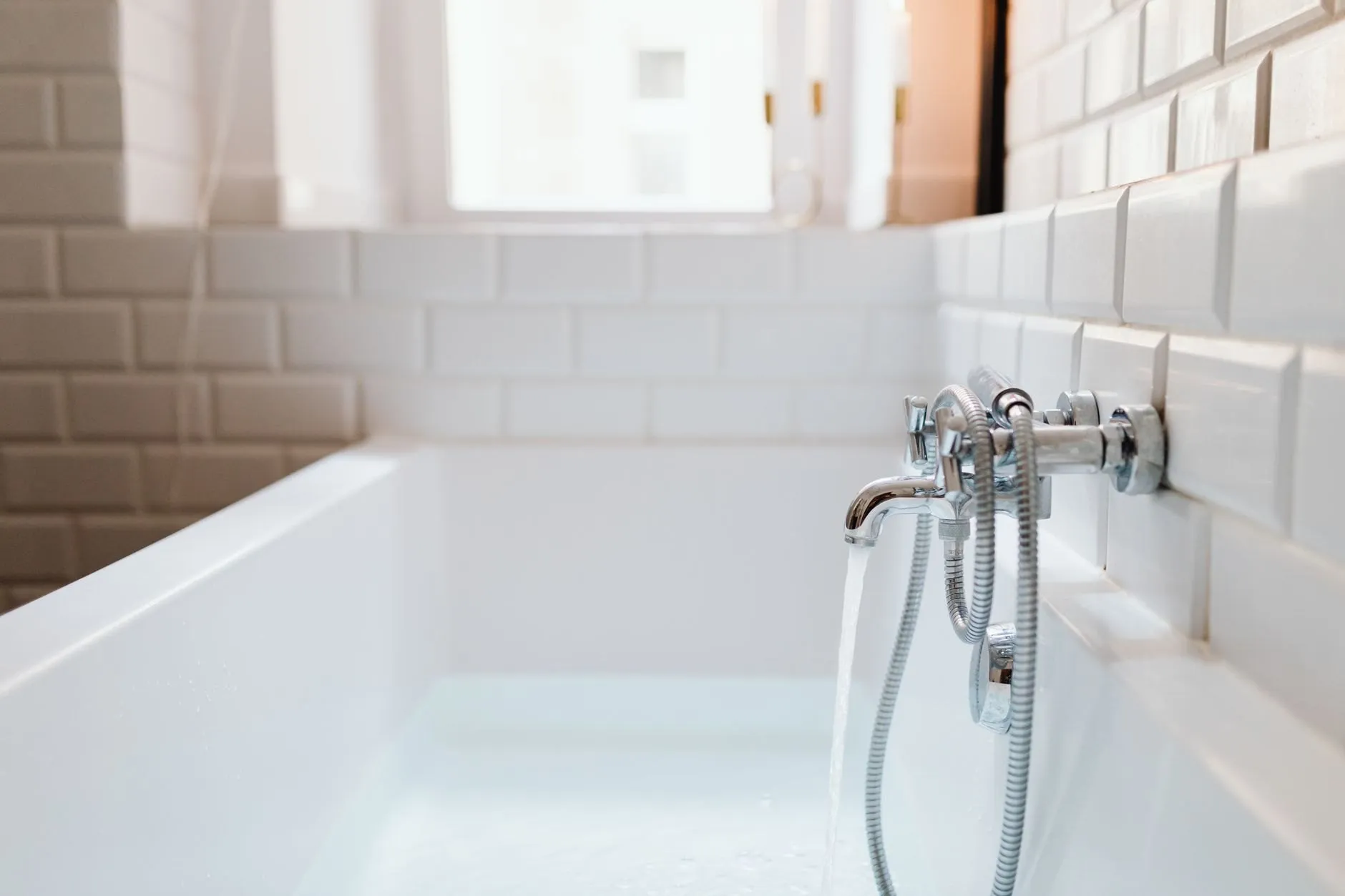 A white bath against white metro tiles with a chrome mixer tap running