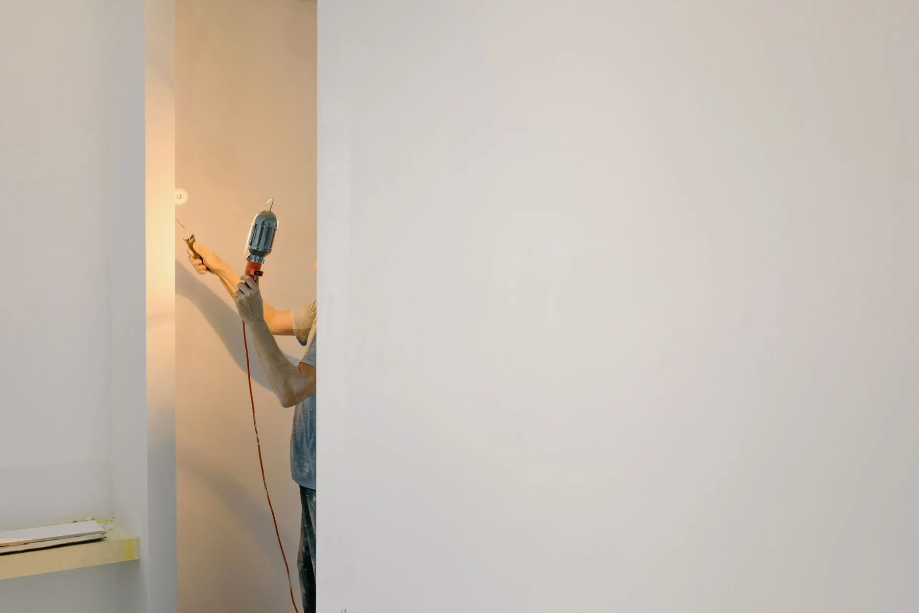 An arm holding a work lamp against a freshly plastered wall in an empty room